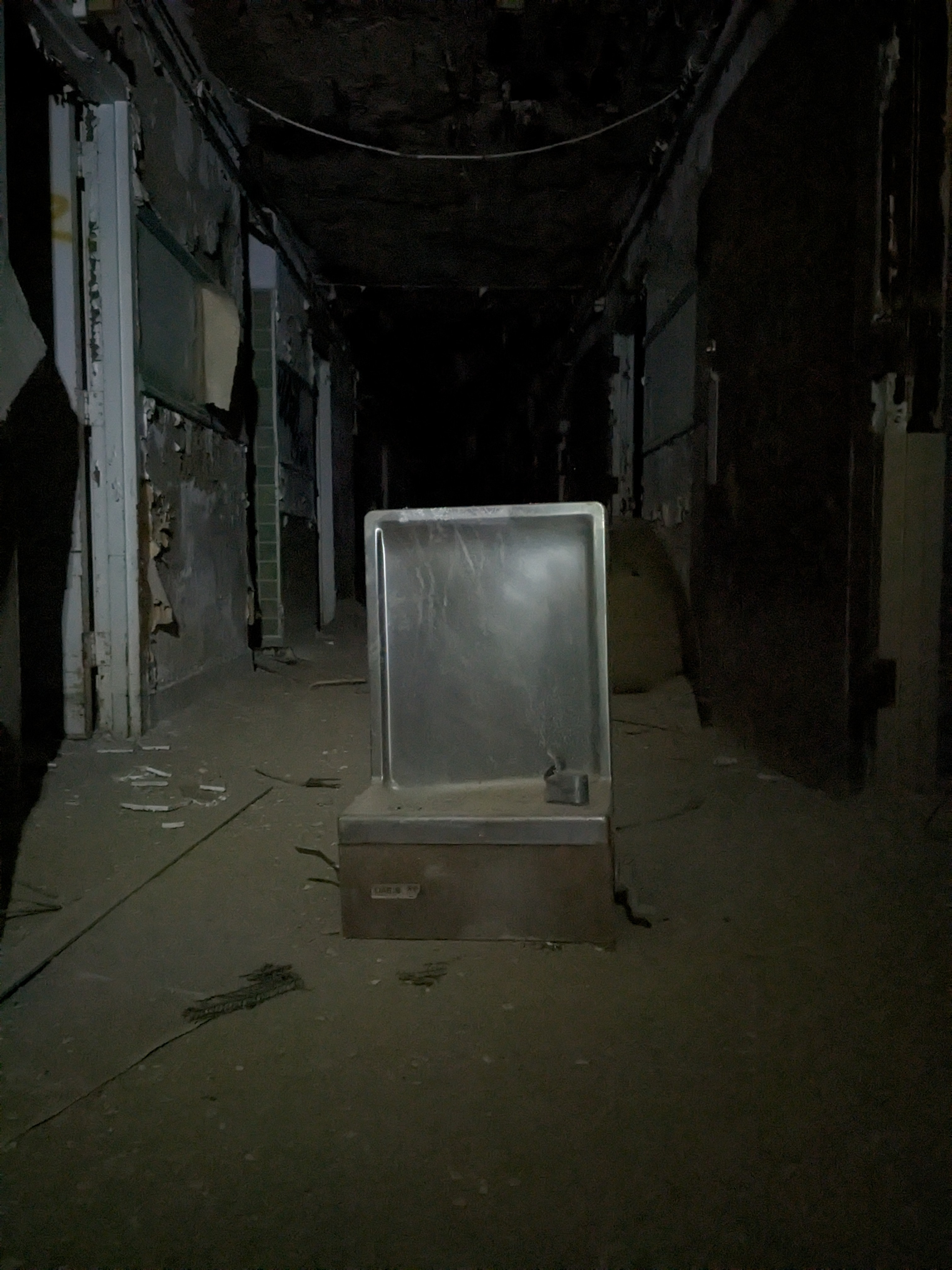 detached drinking fountain placed in the middle of a hallway in an abandoned building