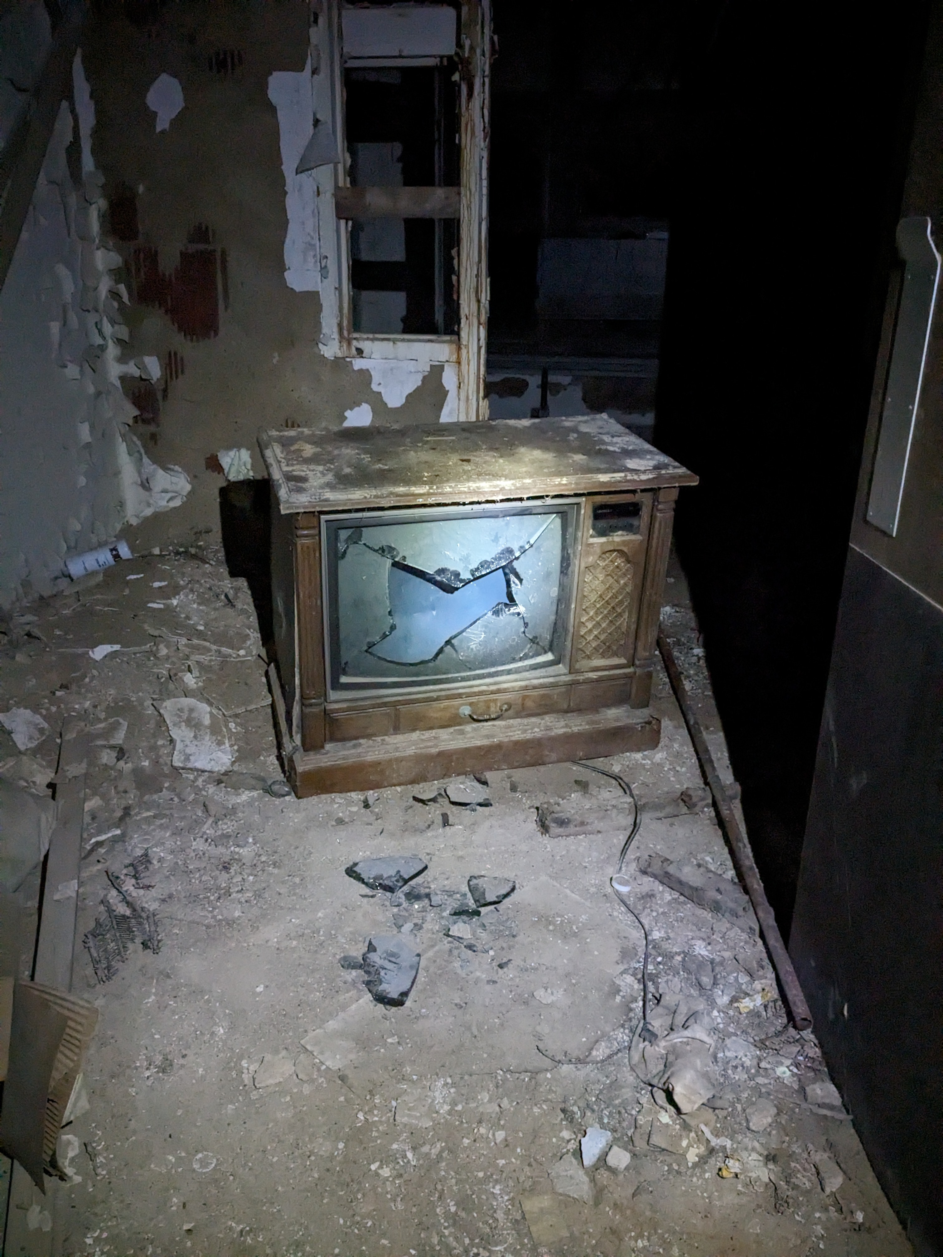 old box tv sitting in the middle of an abandoned asylum room with a smashed screen